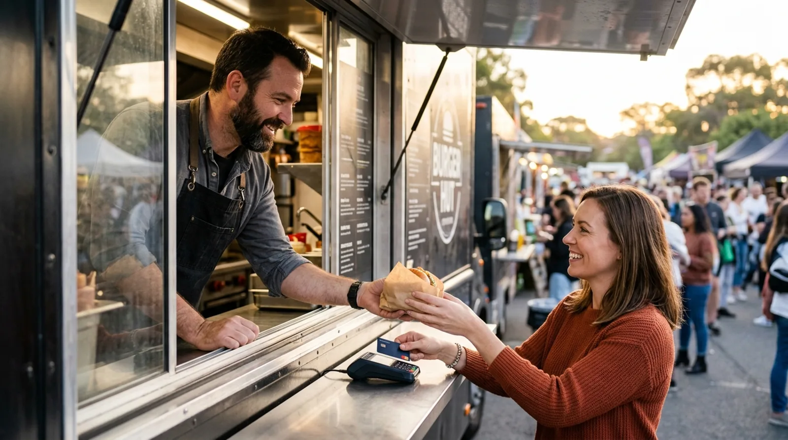 Właściciel food trucka przyjmuje płatność kartą na terminalu podczas obsługi klienta
